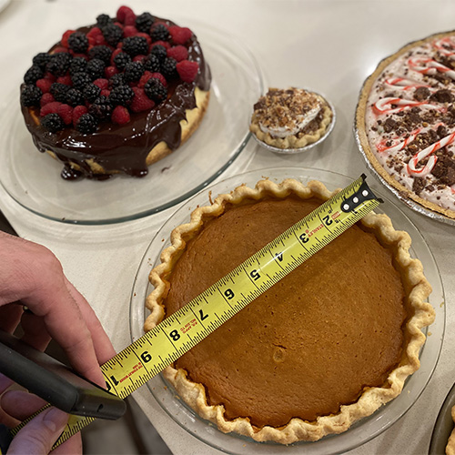 Delicious thanksgiving pies spread out on a counter - a man measures the pumpkin pie with a measuring tape >